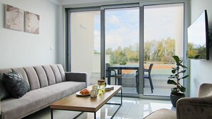 A modern living room with a grey sofa, a wooden coffee table with breakfast items, a glass-top table, and a view of a tennis court through large sliding glass doors. - Phaedrus Living Seaside Executive Flat Harbour 204 (Paphos)