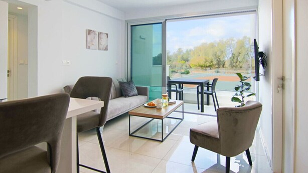A modern living room with a sofa, chairs, a coffee table, and a large sliding glass door leading to an outdoor area. - Phaedrus Living Seaside Executive Flat Harbour 204 (Paphos)