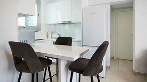 A modern kitchen with white cabinets, a white dining table, and four dark chairs. - Phaedrus Living Seaside Executive Flat Harbour 204 (Paphos)
