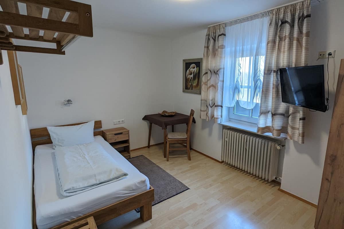 A bedroom with a bed, a desk, a chair, a radiator, and a TV mounted on the wall.