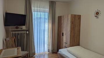 Een slaapkamer met een houten garderobe, een bed, een stoel, een televisie en een raam met gordijnen.