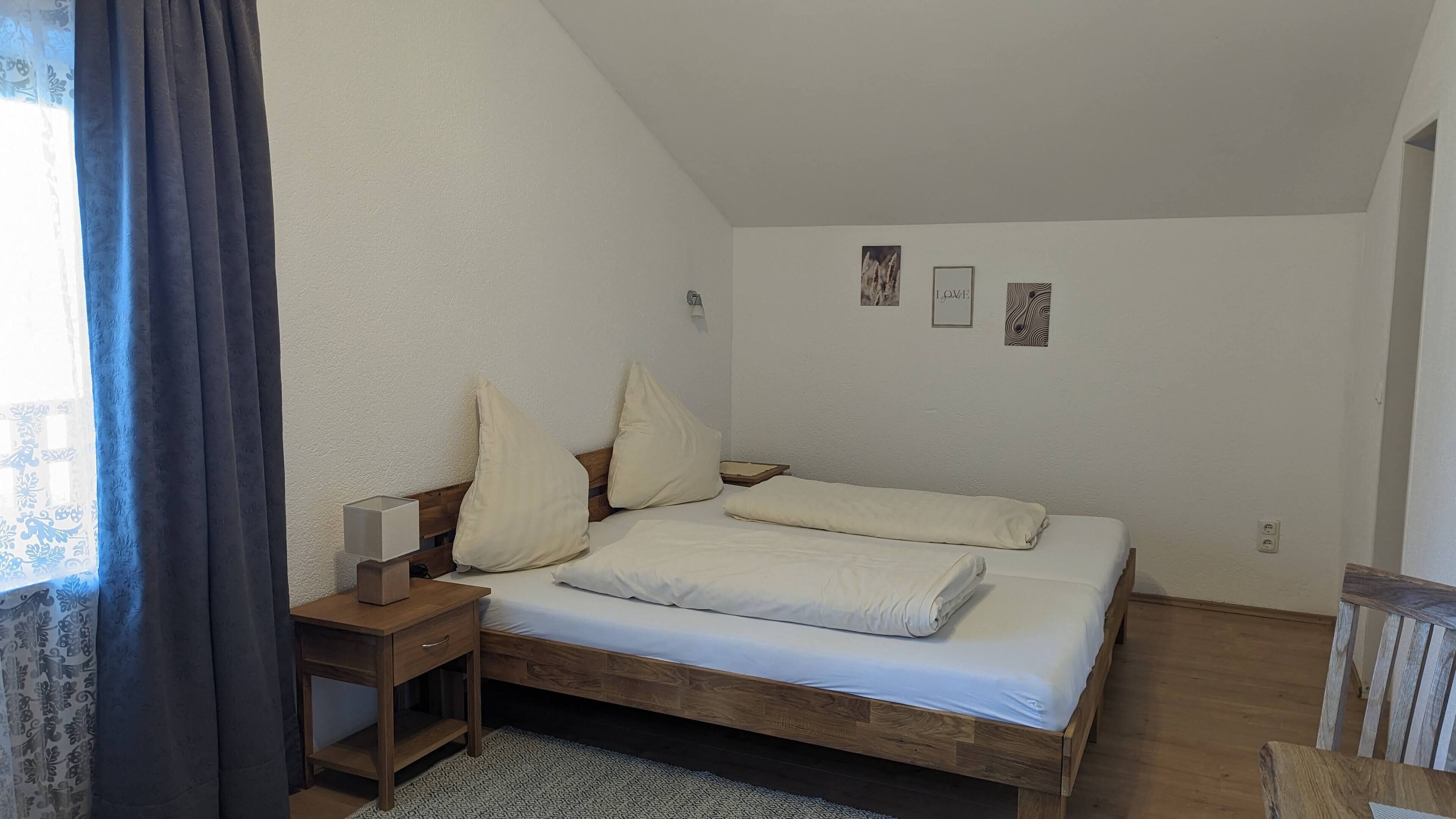 A bedroom with a wooden bed, a nightstand, a lamp, and a window with curtains.