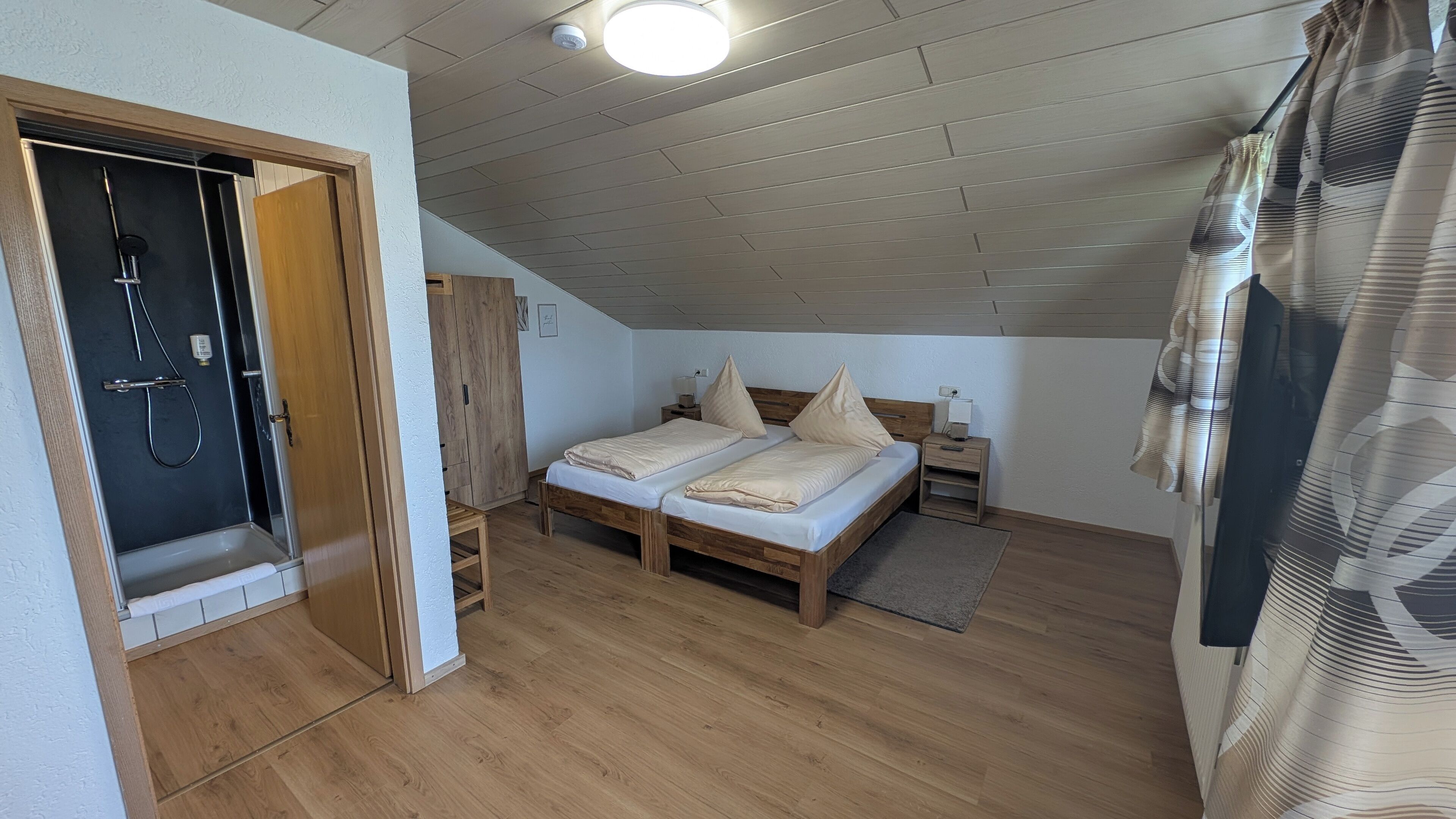 A bedroom with a wooden bed, a nightstand, a bedside table, a wooden wardrobe, and a shower area.