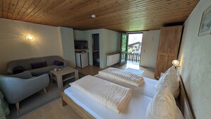 Una habitación acogedora con dos camas, un sofá, una mesita y un pequeño rincón americano.