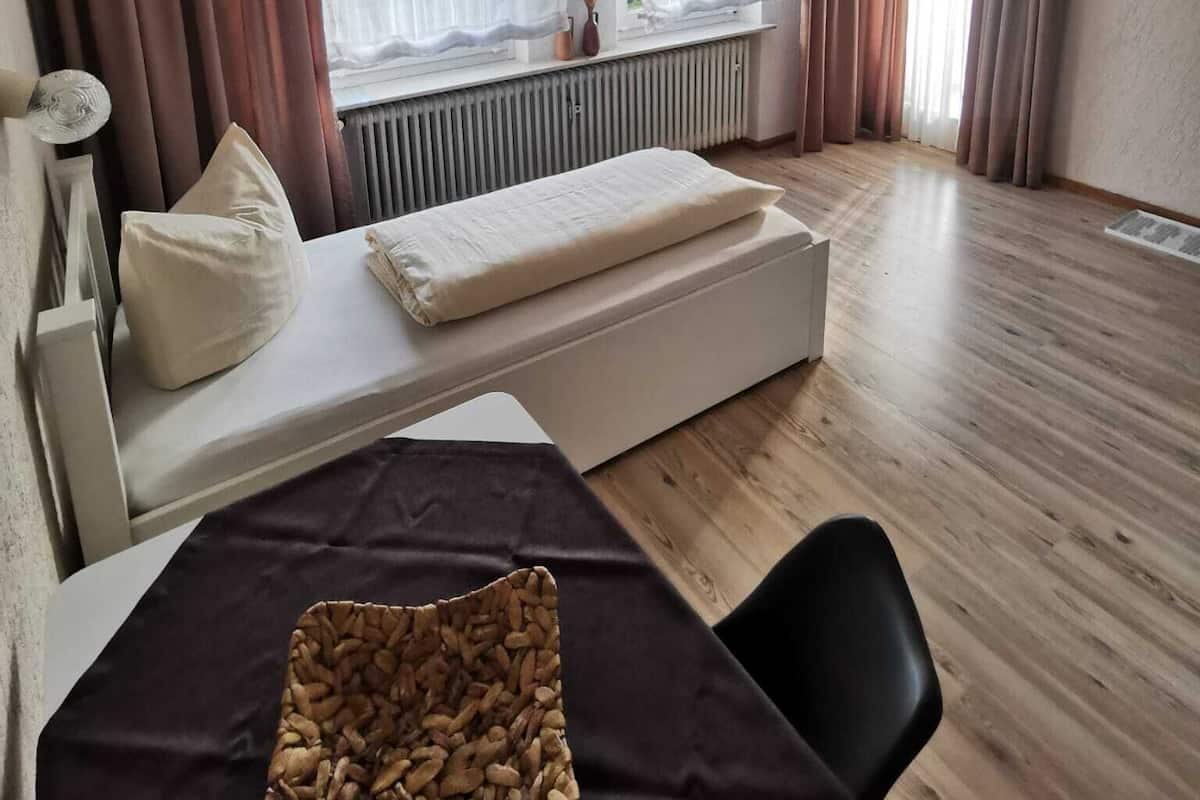A hotel room with a bed, a small table, a chair, a TV, and a window with curtains.