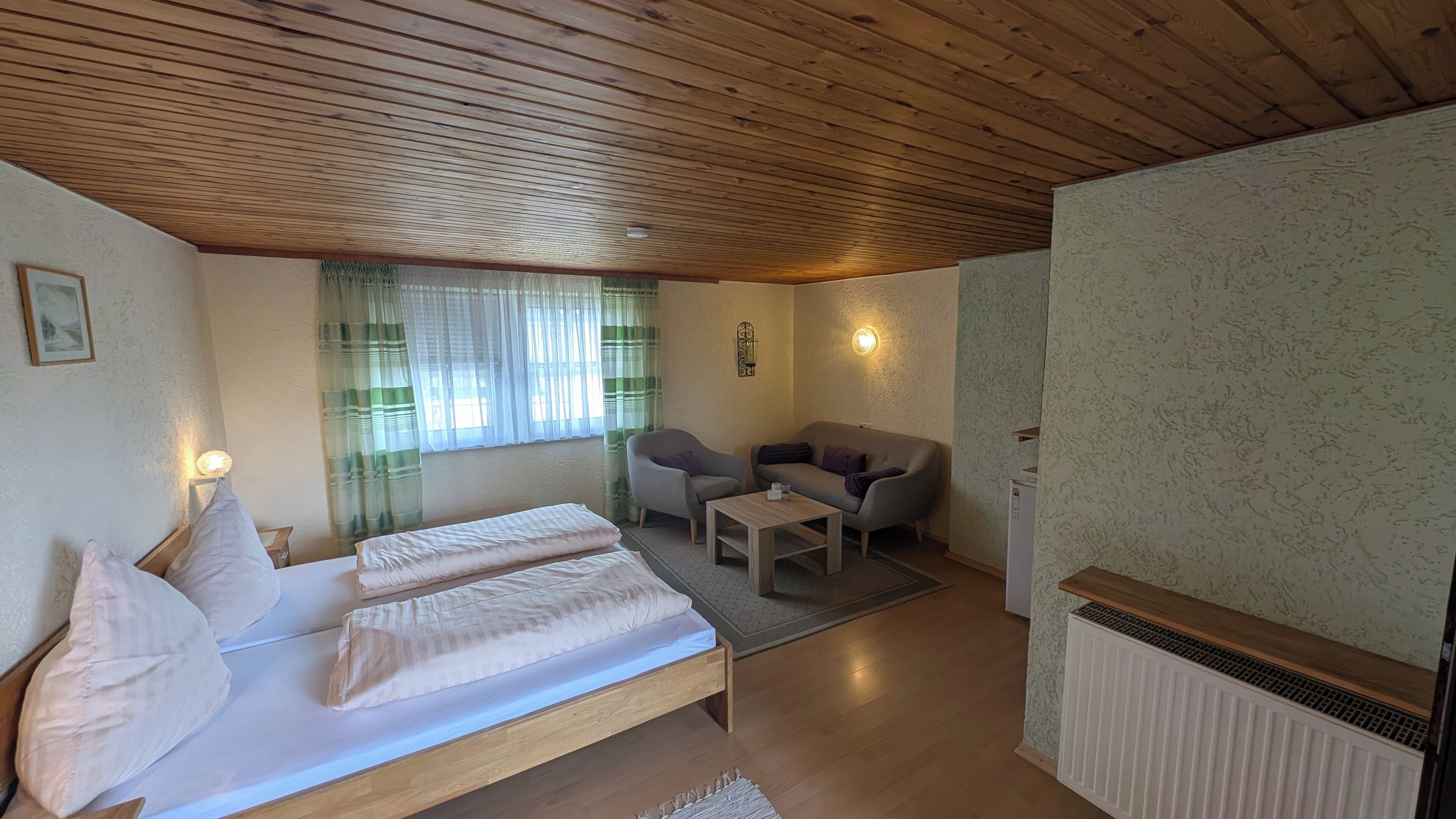 A cozy room with a bed, two chairs, a small table, and a radiator.
