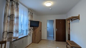 Una habitación con un armario de madera, un televisor montado en la pared, un radiador y una puerta que da a otra habitación.