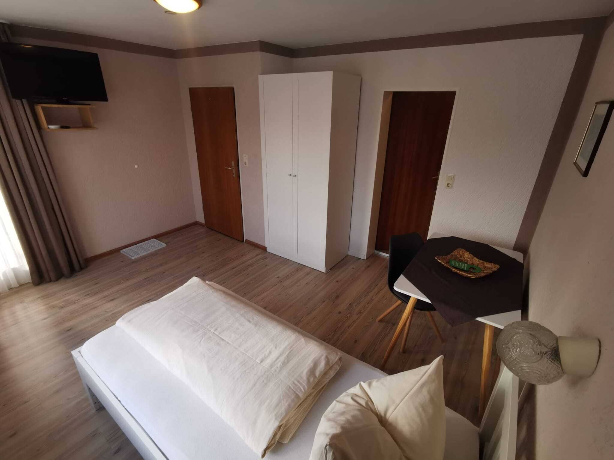 A hotel room with a bed, a desk, a chair, a wardrobe, and a television.