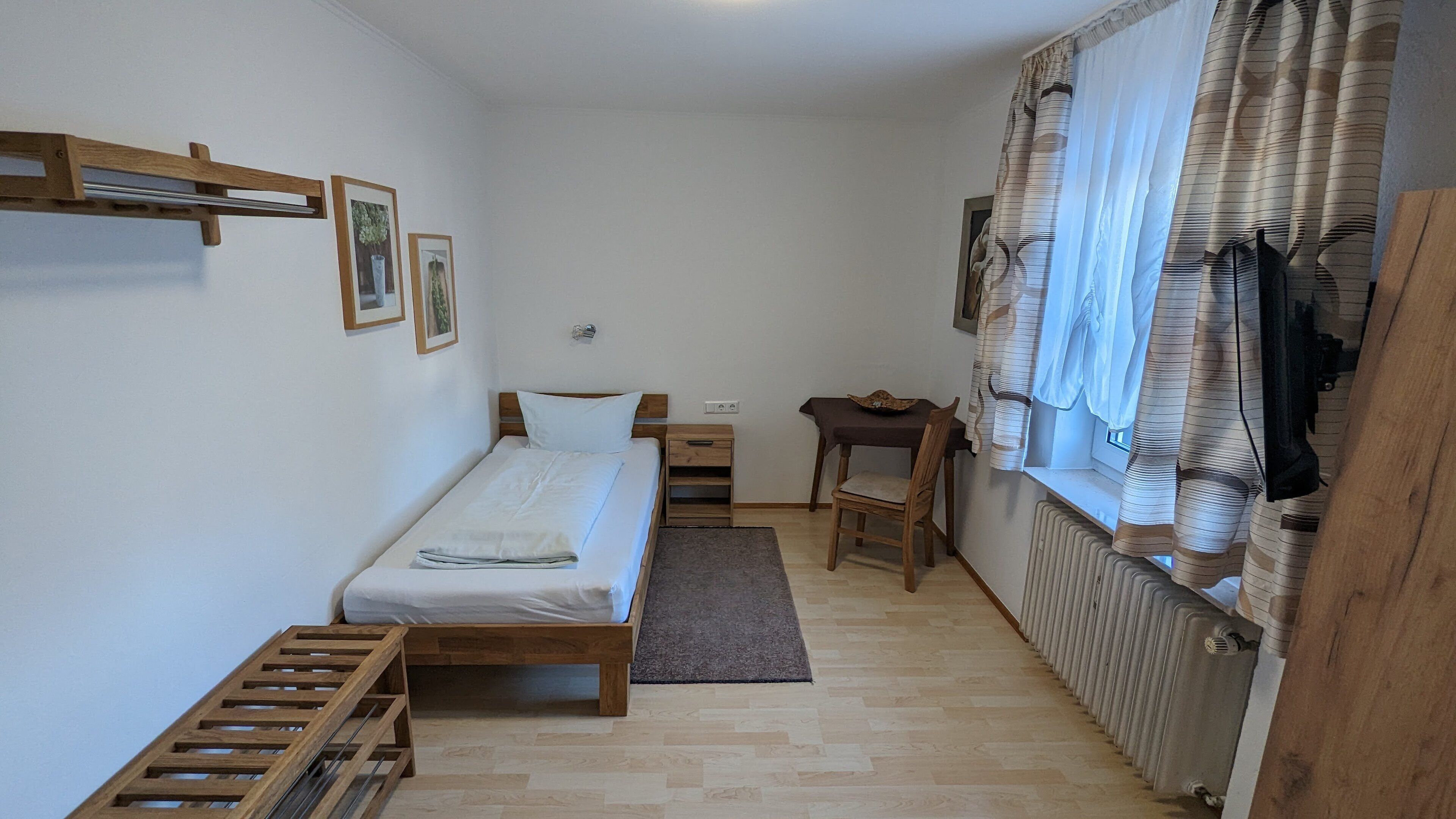 Una habitación pequeña y ordenada con una cama individual, una mesita de noche de madera, una silla y un radiador.