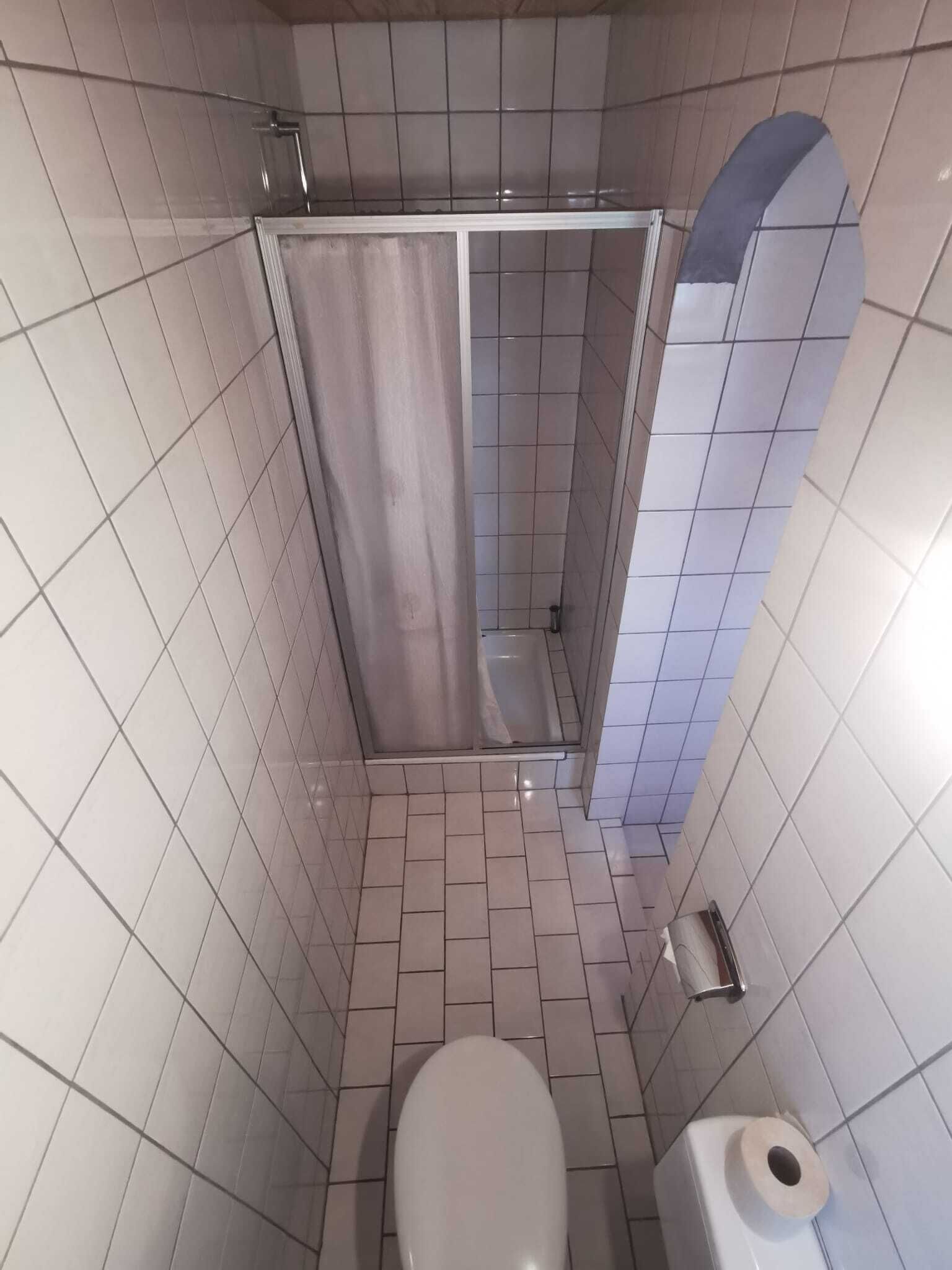 Une petite salle de bain carrelée, équipée d’une douche, de toilettes et d’un distributeur de serviettes en papier.