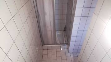Une petite salle de bain carrelée, équipée d’une douche, de toilettes et d’un distributeur de serviettes en papier.
