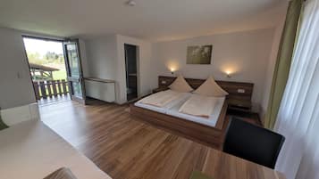 A bedroom with a large bed, wooden headboard, two bedside tables, a nightstand, a radiator, and a view of a deck and outdoor area.