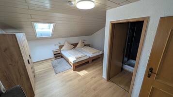 Un dormitorio con techo de madera, tragaluces, cama con almohadas, mesita de noche y puerta que da al baño.