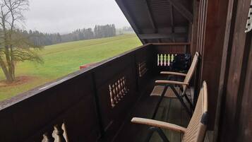 Un balcon en bois avec des chaises en osier, une vue sur un champ verdoyant et un ciel nuageux.