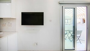 Une cuisine moderne dotée d’un téléviseur à écran plat fixé au mur et d’une porte-fenêtre coulissante donnant sur un espace extérieur aménagé avec des chaises.