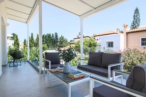 Ein überdachter Außenbereich mit einer Couch, Stühlen und einem Couchtisch.