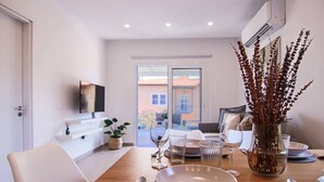 Una zona de menjador amb taula de fusta preparada per a quatre, un vas amb plantes seques i un televisor fixat a la paret.