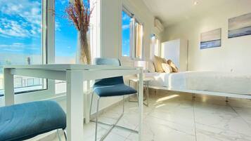Een moderne hotelkamer met een groot raam, een zithoek met een tafel en stoelen, en een bed met een witte hoofdbord.