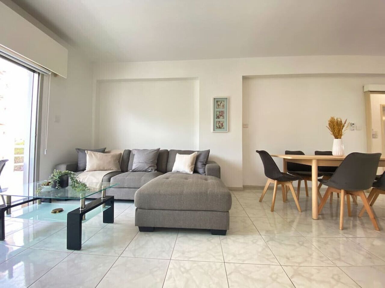 Een moderne woonkamer met een bank, een voetenbankje, een glazen salontafel en een eethoek met een tafel en stoelen.