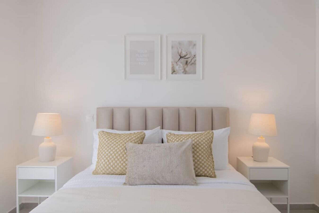 Une chambre à coucher bien rangée, avec un lit, deux tables de chevet et deux lampes fixées au mur.