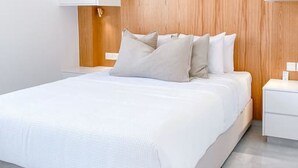 Een moderne slaapkamer met een groot bed, een houten hoofdbord, witte nachtkastjes en een witte garderobe.