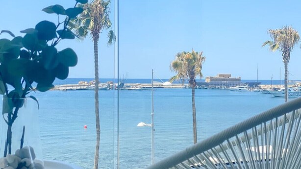 Een balkon met uitzicht op zee, palmbomen en een stoel.