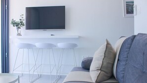 Een moderne woonkamer met een grijze bank, een flatscreen televisie aan de muur en een klein barretje met krukken.