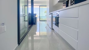 Cozinha moderna com armários brancos, porta de vidro que dá para uma varanda, e vista para o exterior.