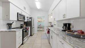 Een moderne keuken met witte kasten, een ingebouwde magnetron, een roestvrijstalen koelkast en een koffiezetapparaat.