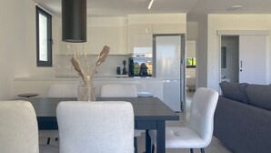 Una cucina moderna con mobili bianchi, un tavolo da pranzo con sedie e un divano grigio nella zona giorno.