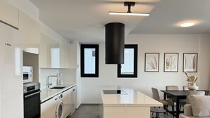 A modern kitchen with a central island, a dining area with a table and chairs, and a sofa. - Phaedrus Living: White Hills Suites City View (Aglantzia)