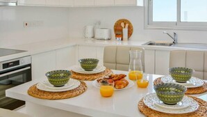 A modern kitchen with white cabinetry, a dining table set with green bowls, plates, and orange juice. - Phaedrus Living: Seaside Luxury Flat Lighthouse 67 (Paphos)