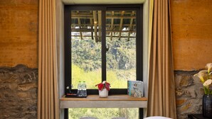 A room with a bed, a window with a view of greenery, a shelf with a vase and books, and a small table with bottles. - Sapaxa Spring Garden Ecolodge (Ta Phin)