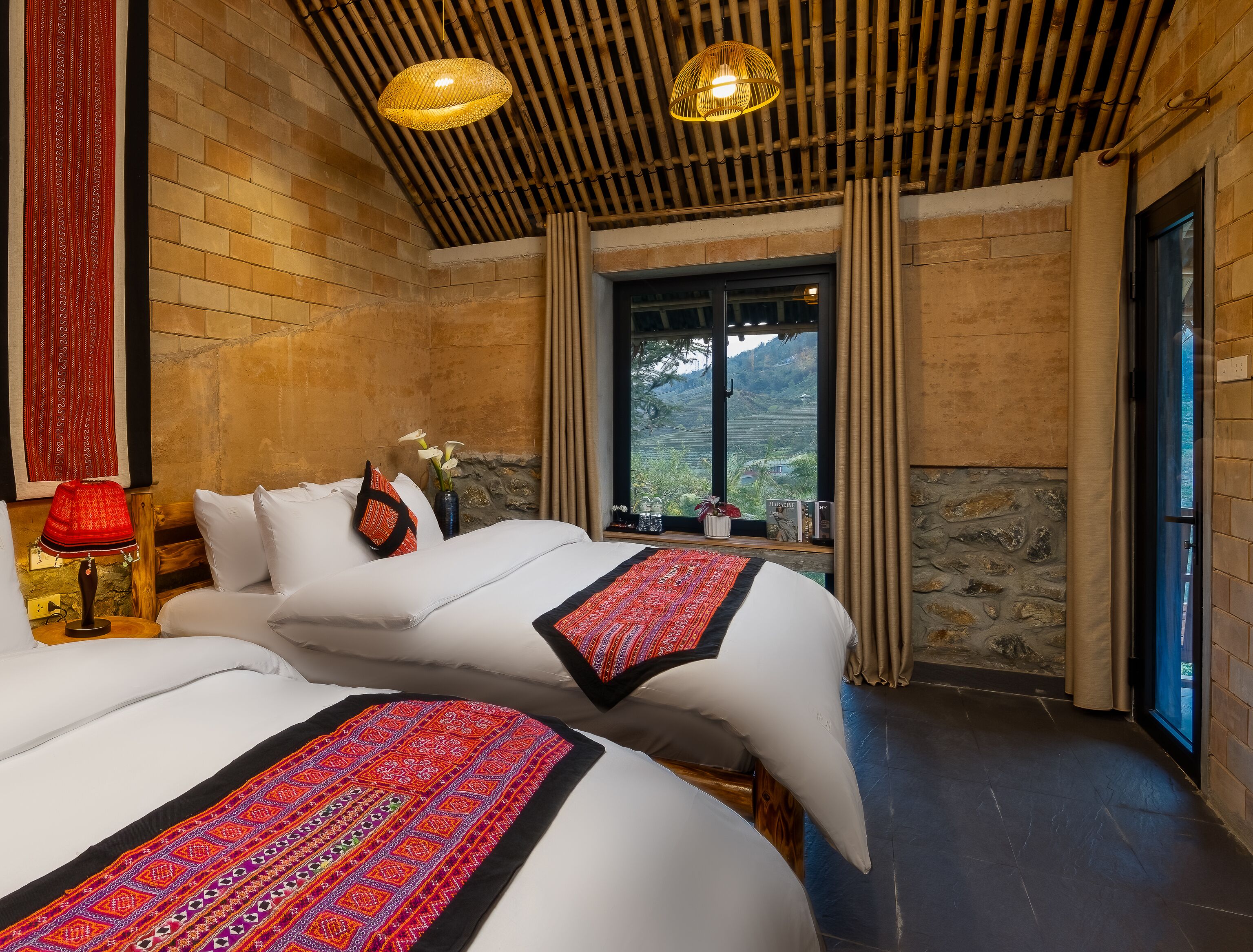 A room with two beds, a large window with a view, a bamboo ceiling, and a red patterned rug.