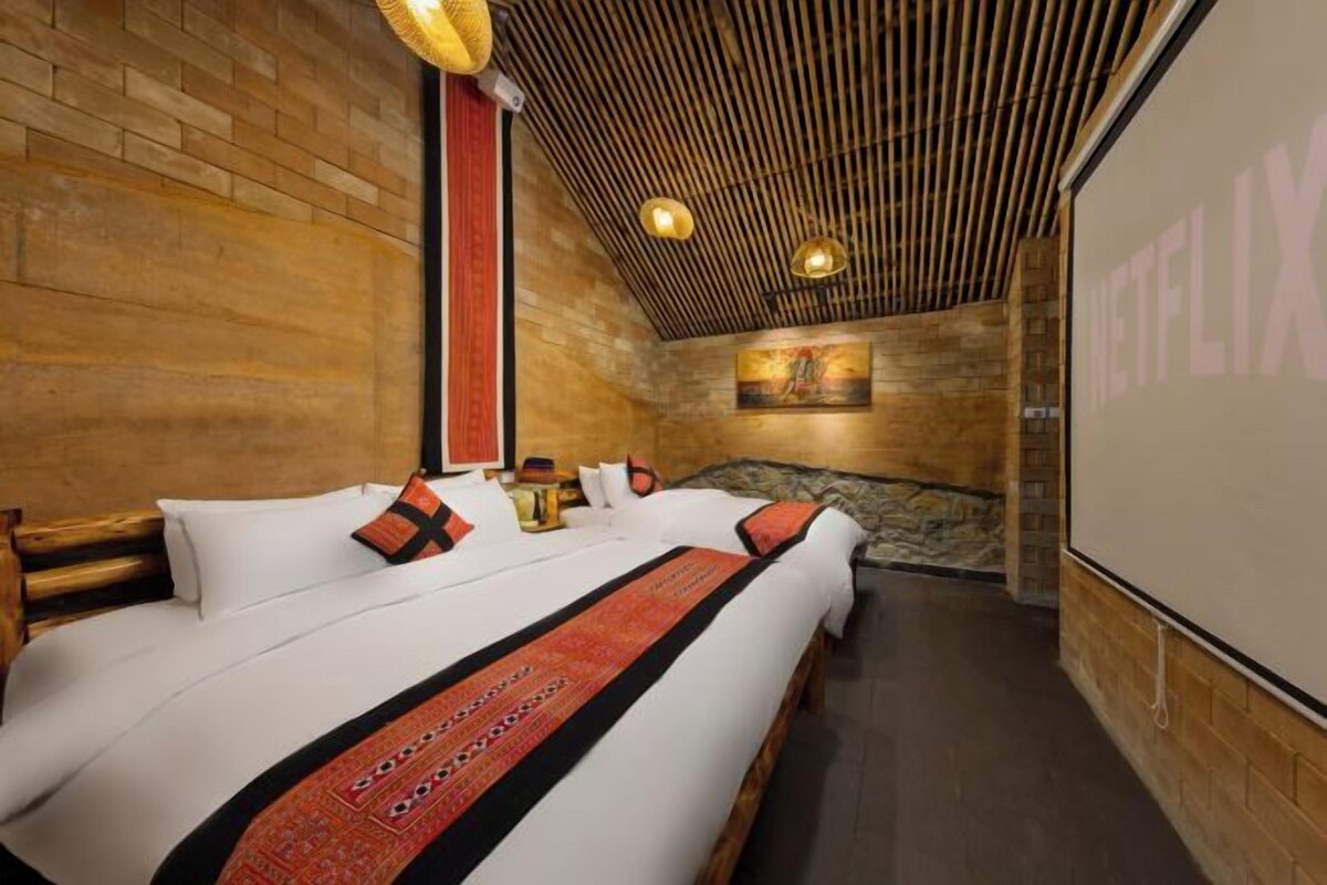 A hotel room with a large bed, a wooden ceiling, and a wall-mounted screen.
