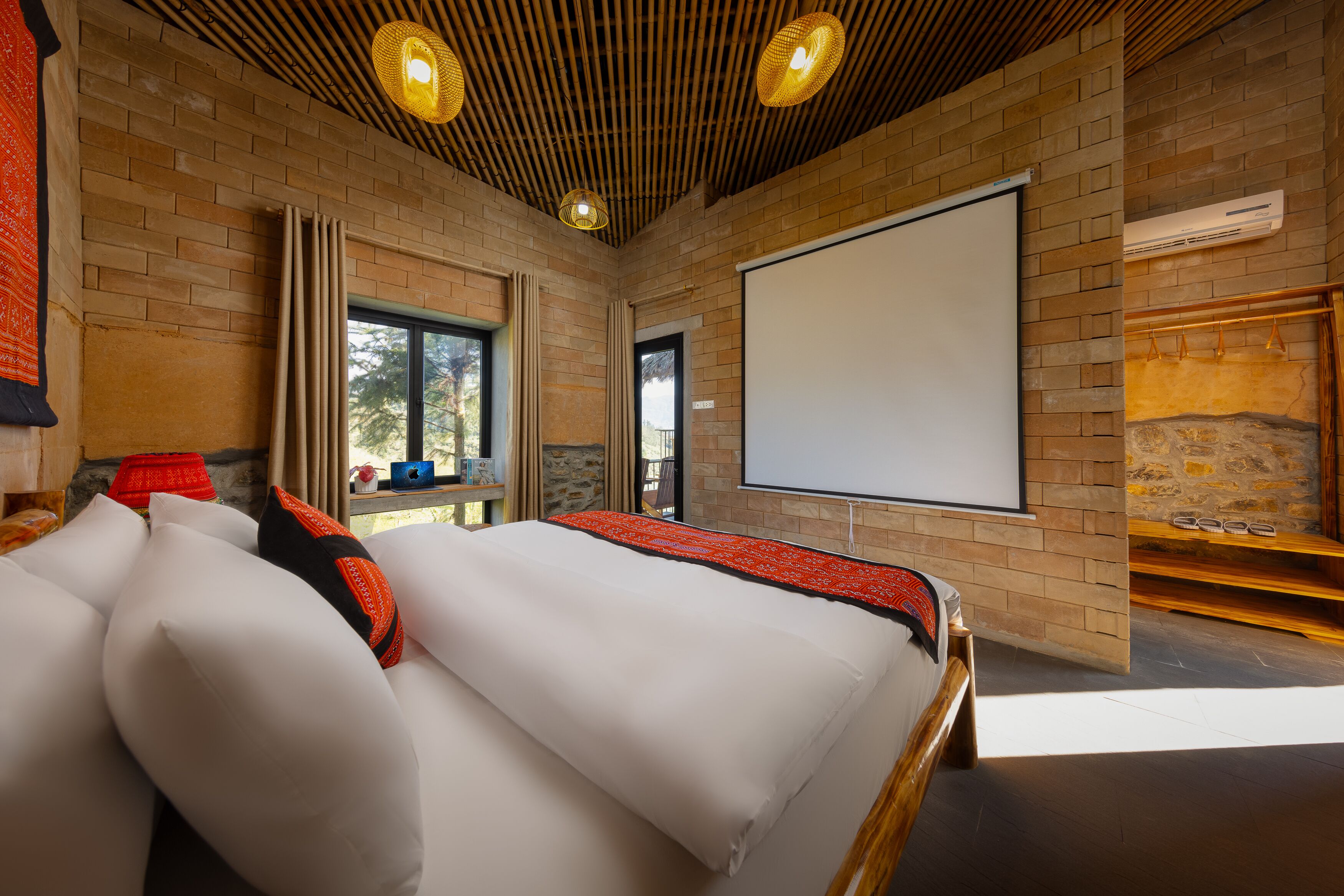A modern hotel room with a large bed, a projector screen, and a stone wall.