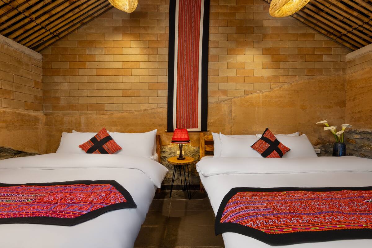 Una habitación con dos camas, una mesita y un tapiz rojo y negro a rayas.