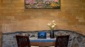 A room with a stone wall, a painting of a landscape, a laptop, and two chairs.
