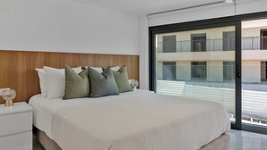 Et moderne hotelværelse med en stor seng, et træhovedgærde og en skydedør, der fører ud til en balkon med udsigt over byen.