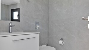 Et moderne badeværelse med en hvid kommode, toilet og spejl.