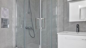 Un baño moderno con ducha envuelta en vidrio, un lavabo blanco y un espejo sobre él.