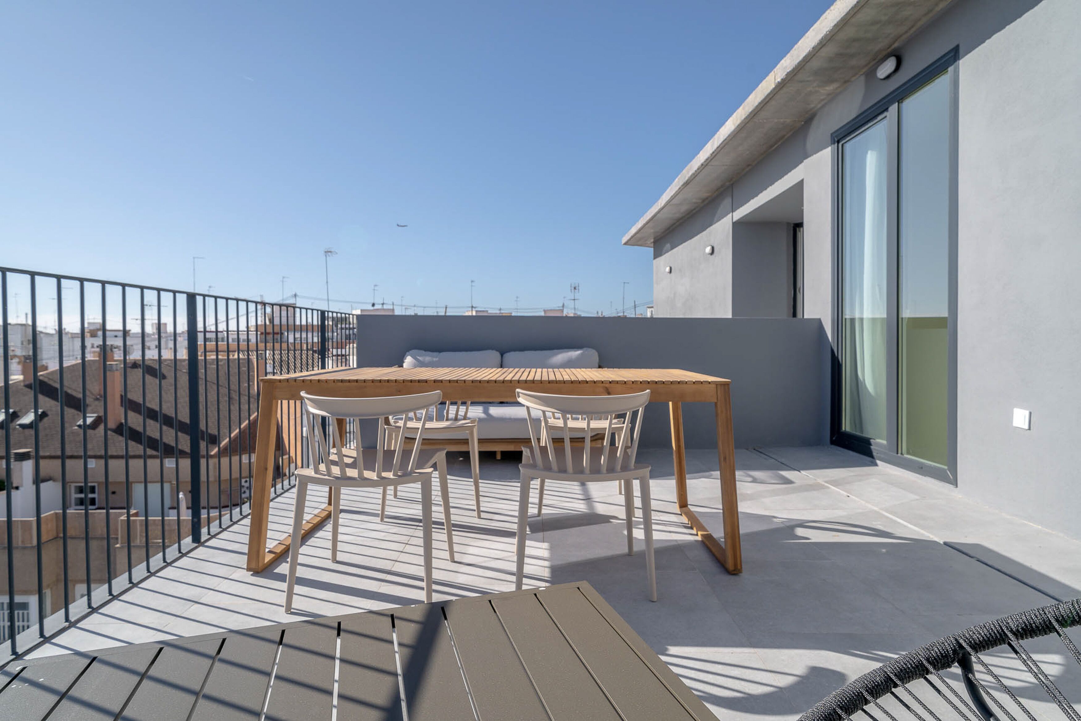 A rooftop terrace with a wooden table and chairs, a glass door, and a view of the cityscape.