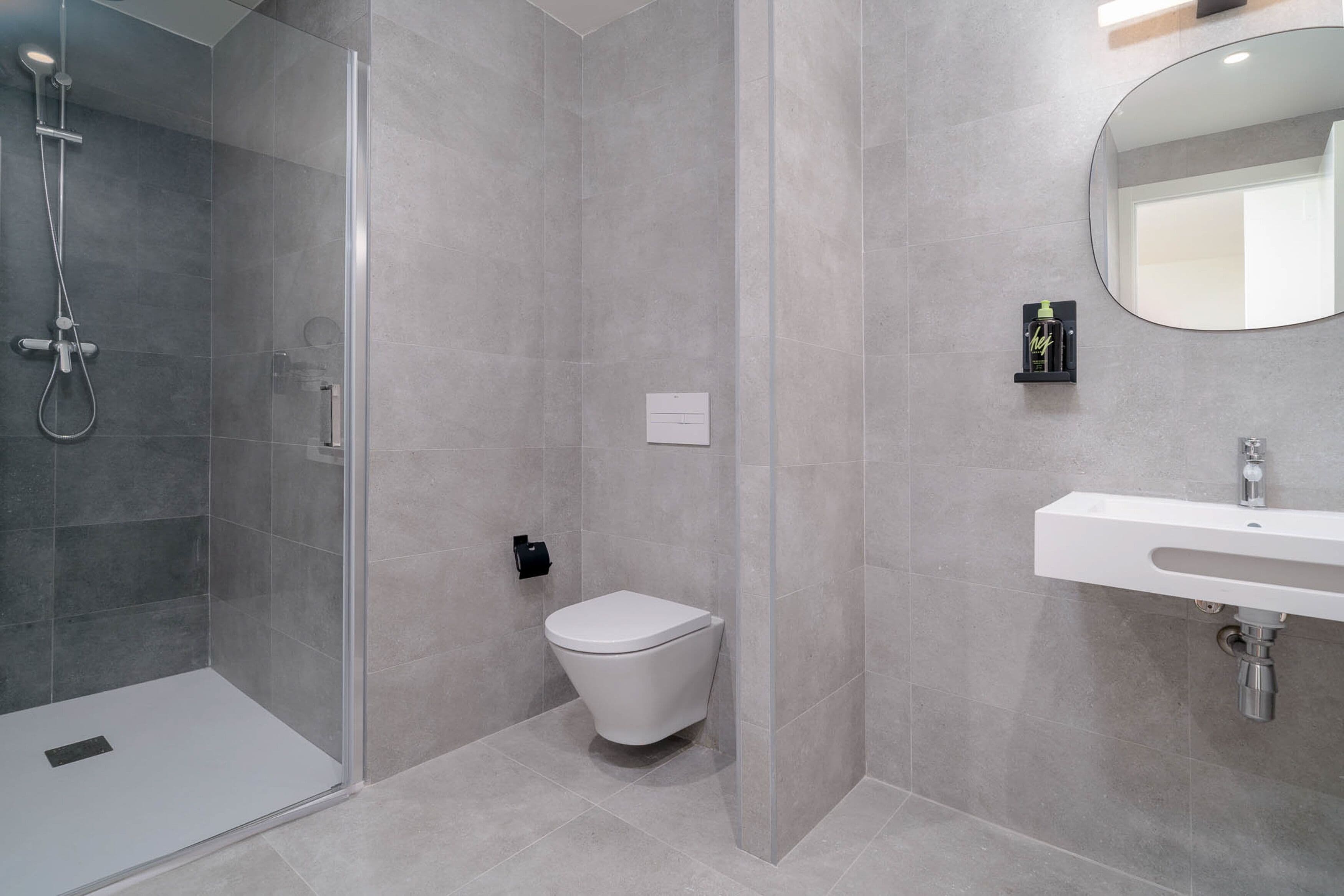 A modern bathroom with a glass-enclosed shower, a white toilet, and a sink with a mirror.
