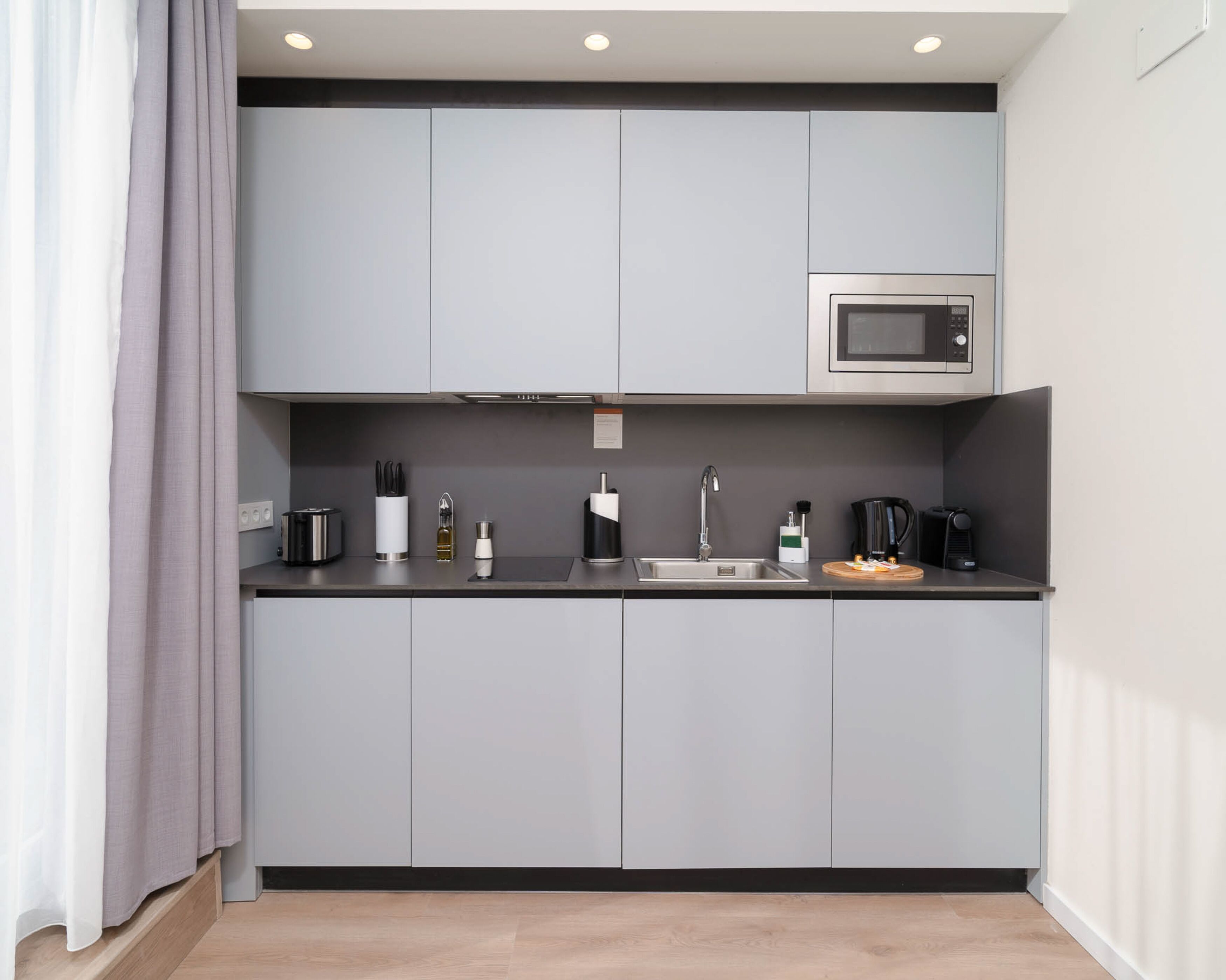 Een moderne keuken met grijze kastjes, een RVS magnetron en een spoelbak.
