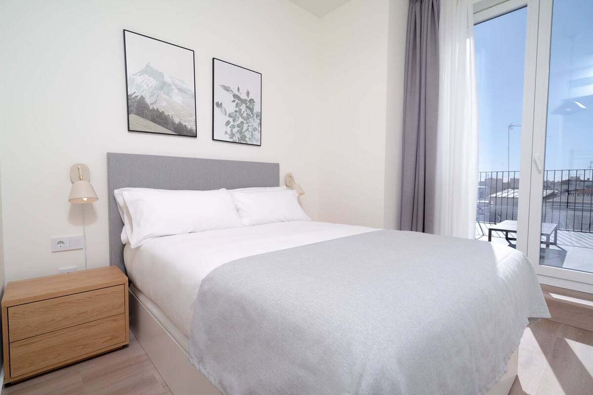 Un dormitorio ordenado con cama, mesitas de noche y ventana con vistas.