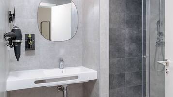 Un baño moderno con un lavabo blanco, un espejo redondo y una ducha con cerramiento de vidrio.