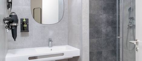 Un baño moderno con un lavabo blanco, un espejo redondo y una ducha con cerramiento de vidrio.