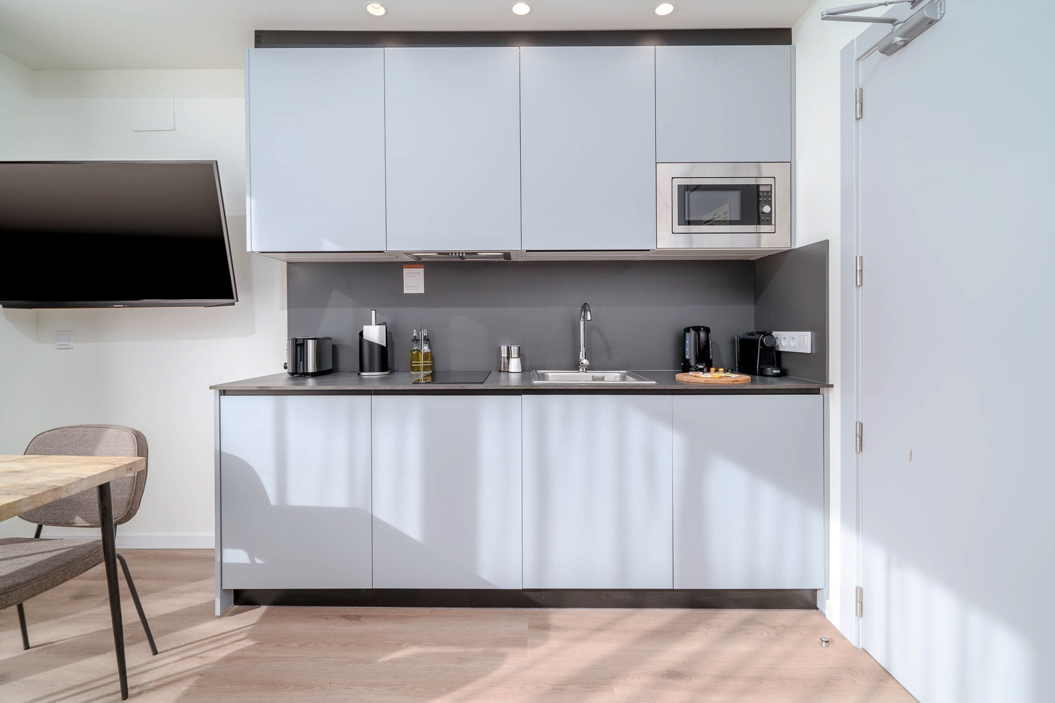 Una cocina moderna con armarios grises, microondas, pileta y televisor de pantalla plana.