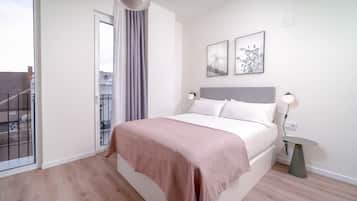 Une chambre à coucher comprenant un lit, une table de chevet, une lampe, une fenêtre avec des rideaux et deux tableaux encadrés accrochés au mur.