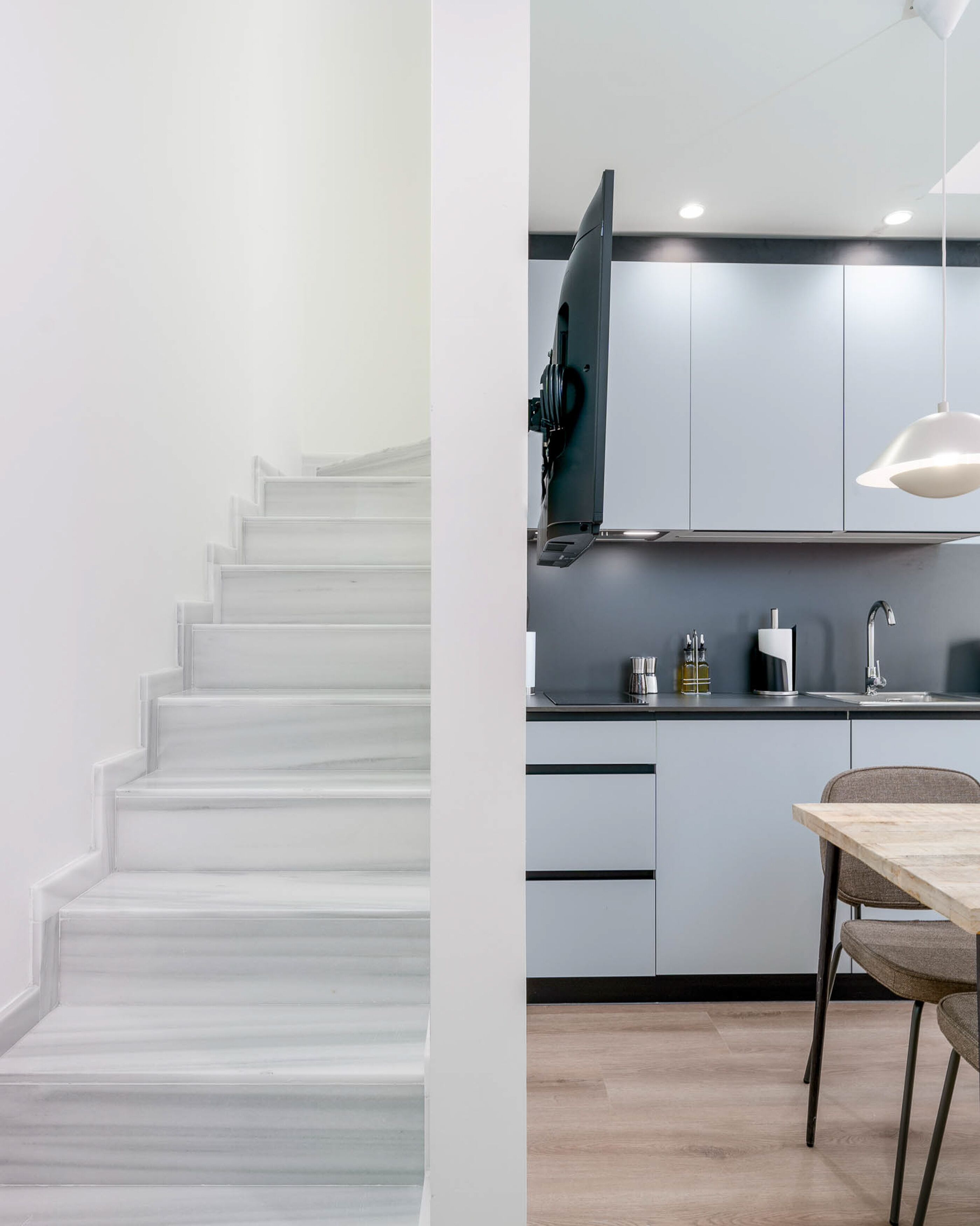 A modern kitchen with grey cabinets, a built-in oven, and a wooden dining table.